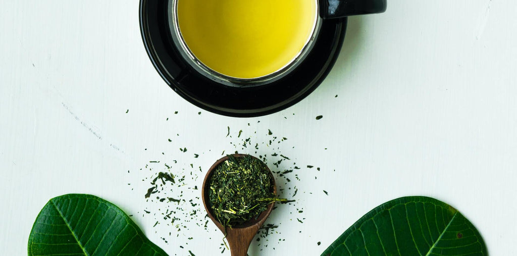 A spoon with tea leaves near the mug with green tea