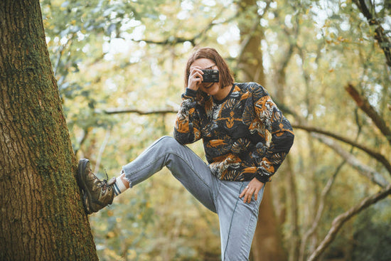 person holding 35mm film camera pointed at the camera with the ocean in the background