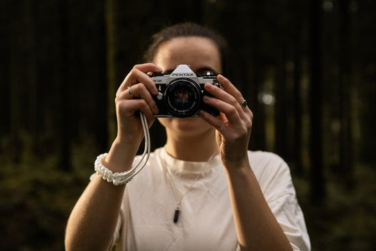 La personne tient un appareil photo argentique Pentax ME Super 35 mm devant son visage.