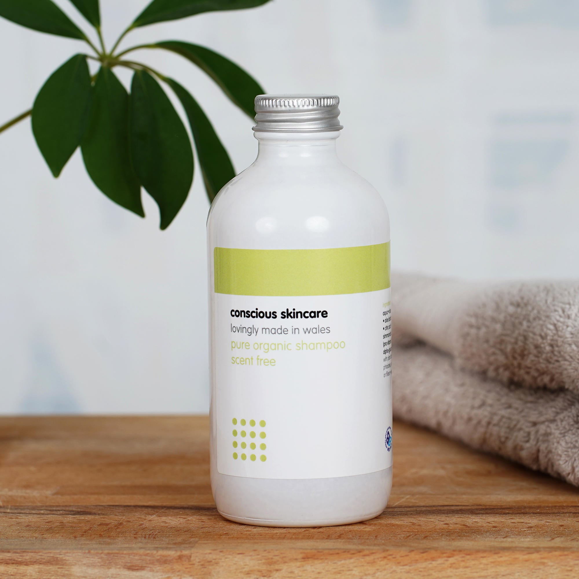 Fragrance Free Shampoo in white glass bottle on wooden table with towel and plant in background