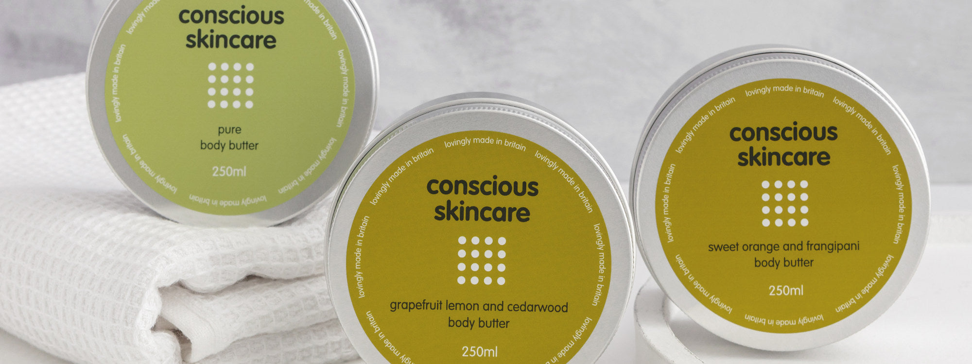 Pure fragrance free body butter along with scented body butters in silver aluminium tins on white table