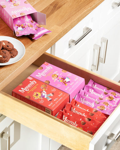 A picture of a wooden shelf containing small packets of mmmly cookies 2 flavors