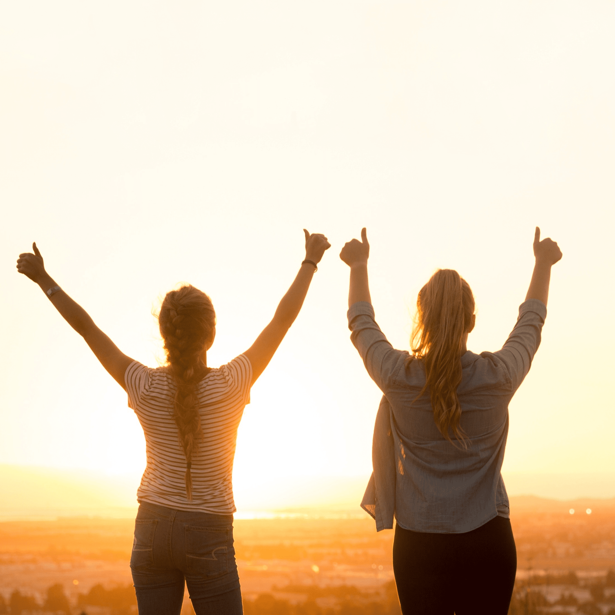 Women with their backs turned, thumbs up in the air illuminated by the sunrise