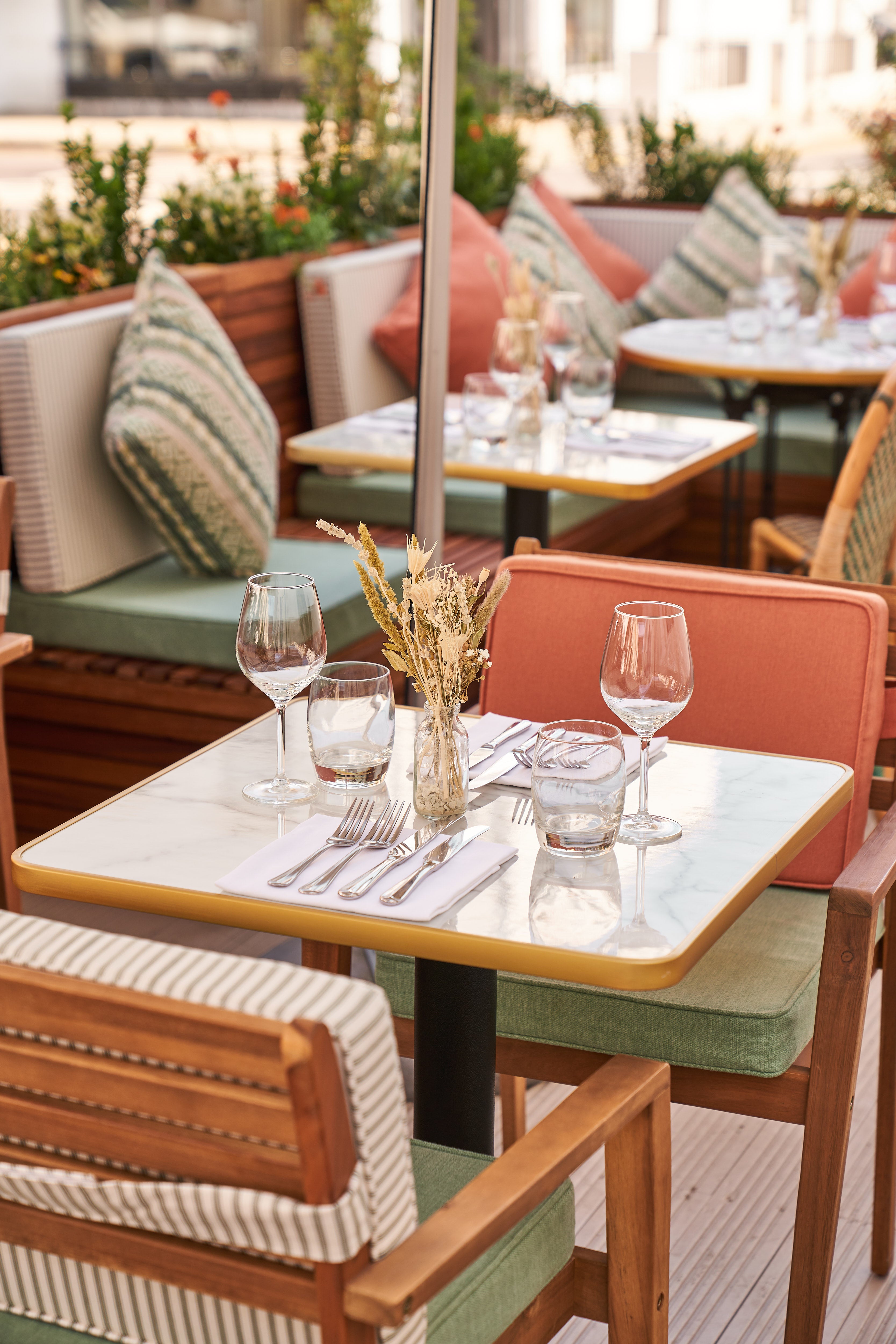 An outdoor seating area for a busy London restaurant. We can see seat cushions with straps as well as bigger bench cushions and scatter cushions for the backs of the bench area. The cushions are made up in shades of green, cream and terracotta.