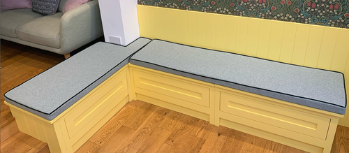 A brightly coloured, daffodil yellow kitchen seating area with two custom shaped bench cushions in a light green fabric with dark green velvet contrast piping.