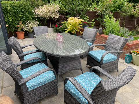 An outdoor table and chairs set in a mid grey wicker. Each chair has a blue and white 60's inspired Orla Kiely fabric cushion, shaped to perfectly fit the seat of the chairs.