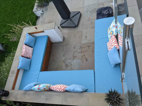 A large outdoor seating area in a garden patio. There are three large foam bench cushions, each made to measure in a sky blue water resistant, hard wearing outdoor upholstery fabric.