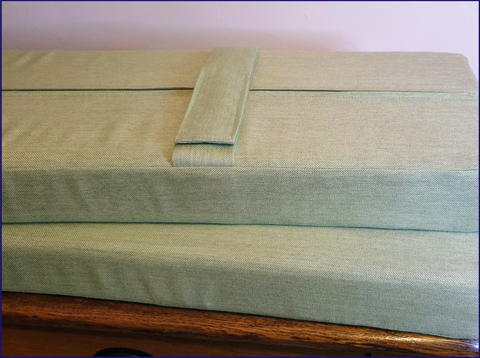 A pair of firm foam outdoor bench cushions covered in a light green water resistant outdoor fabric. Both cushions have 5cm wide velcro straps on to keep the cushions firmly attached to the benches.