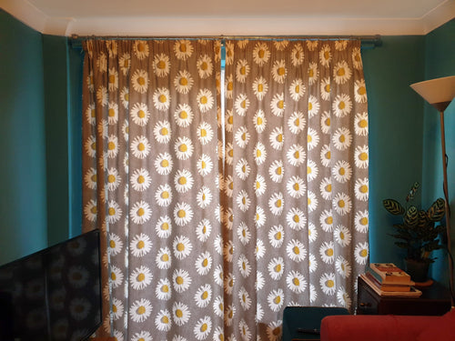 A pair of dairy floral design cotton curtains made by hand. They are floor length french window curtains and have a cotton lining. The curtains sit on a chrome curtain pole and have a pencil pleat heading tape.