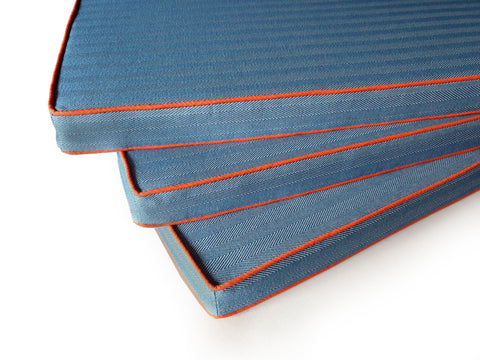 Three made to measure outdoor bench cushions in mid blue herringbone fabric with contrasting bright vibrant orange piping on the top and bottom edges of the cushion.