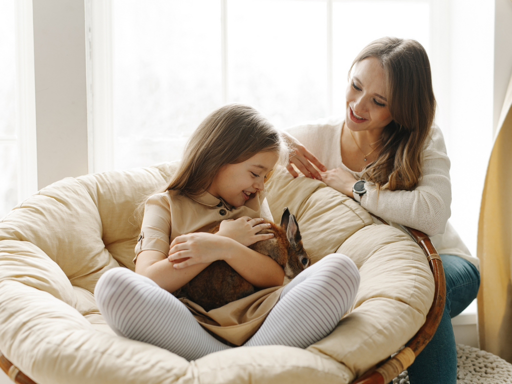 Girl holding her pet rabbit sitting next to her mom