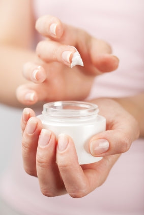 woman holding glass container with lotion on her finger