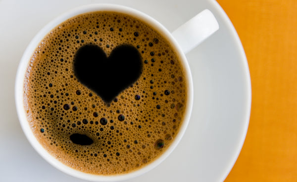 A white coffee cup with a heart-shaped foam design on a saucer against an orange background.