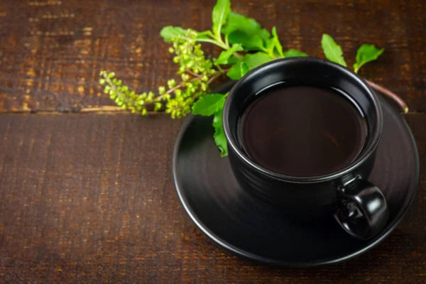 Black cup of coffee with a saucer and fresh green leaves on a dark wooden surface.