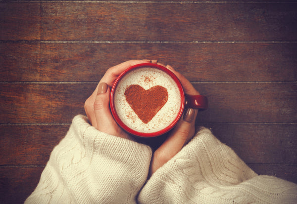 Hands holding a mug of coffee with a heart-shaped latte art, resting on a wooden table.