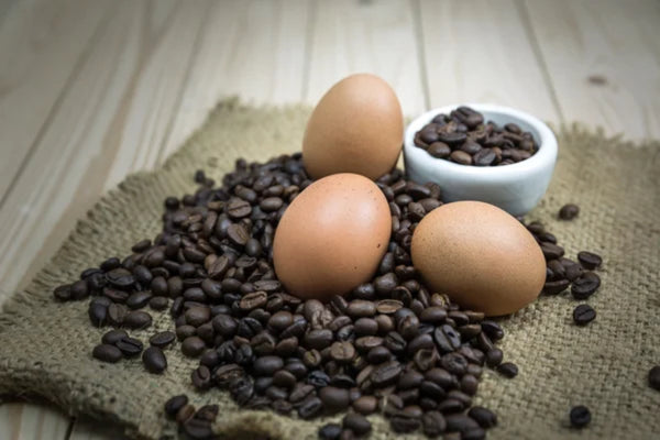 Eggs on a burlap cloth surrounded by scattered coffee beans with more beans in a small white bowl.