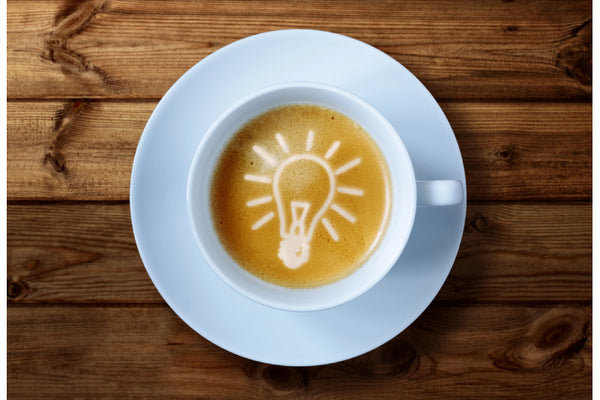 A cup of coffee with a light bulb latte art design on a wooden surface.
