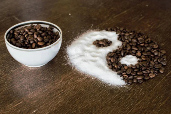 A yin-yang symbol made with coffee beans and salt/sugar on a wooden surface.