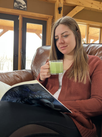 girl sitting on a couch drinking a cup of matcha while reading a book. she is calm and relaxed