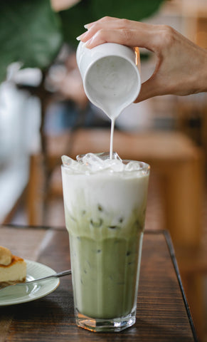 milk being poured over top of matcha in a glass