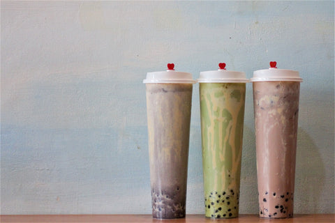 matcha boba (matcha milk bubble tea) in a tall plastic cup with a straw with other types of bubble tea