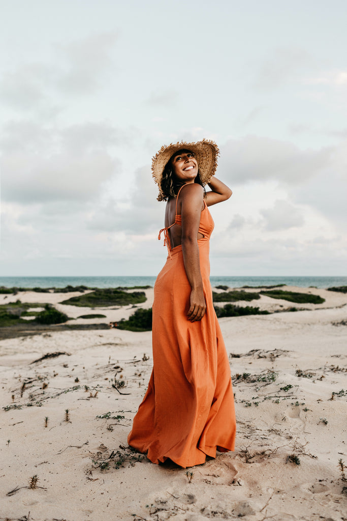 woman wearing an orange maxi dress and sun hat on the beach
