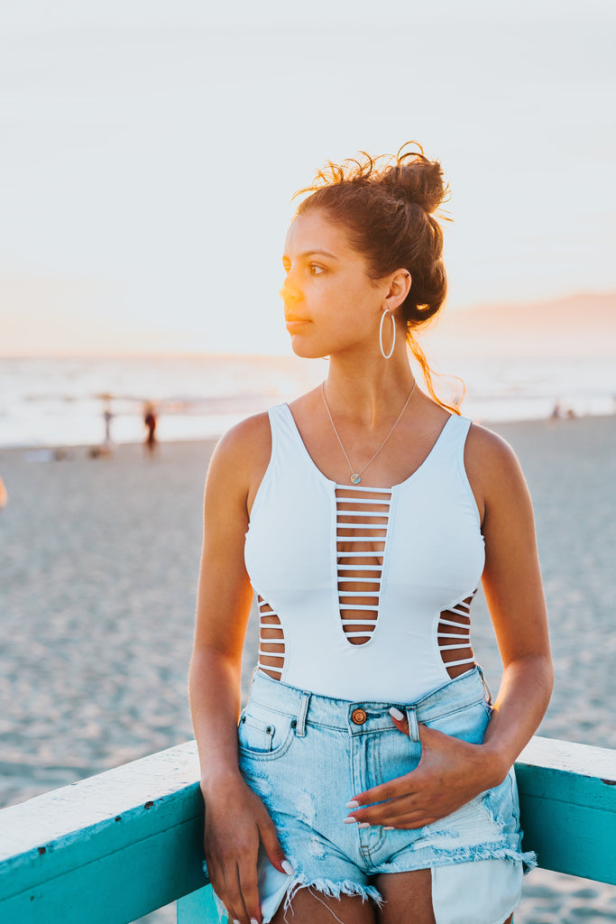 woman wearing a white swimsuit with denim shorts on the beach