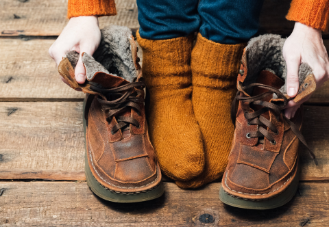Woman's feet wearing orange wool socks next to a pair of winter boots.