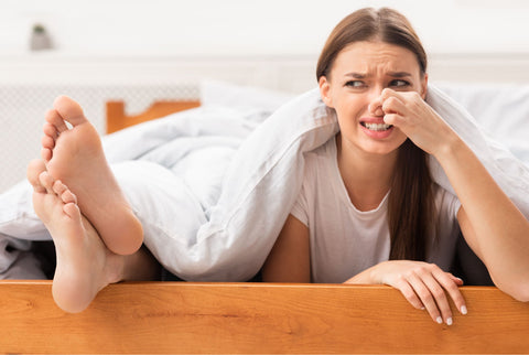 Women laying in bed disgusted by stinky men's legs out of blanket
