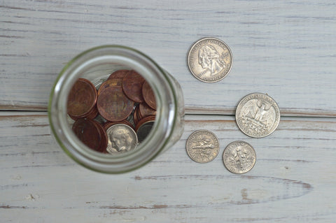 Various coins in a jar with quarters on the table next to it