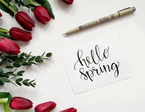 "Hello spring" written in calligraphy with red tulips surrounding the left side