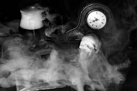 Ein Totenkopf, ein antikes Buch und eine Tisch-Uhr in einer gruseligen Nebelkulisse