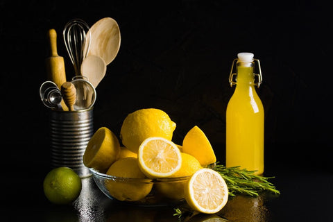 Limoncello traditionnel dans une bouteille avec un bol de citrons et des ustensiles de cuisine.