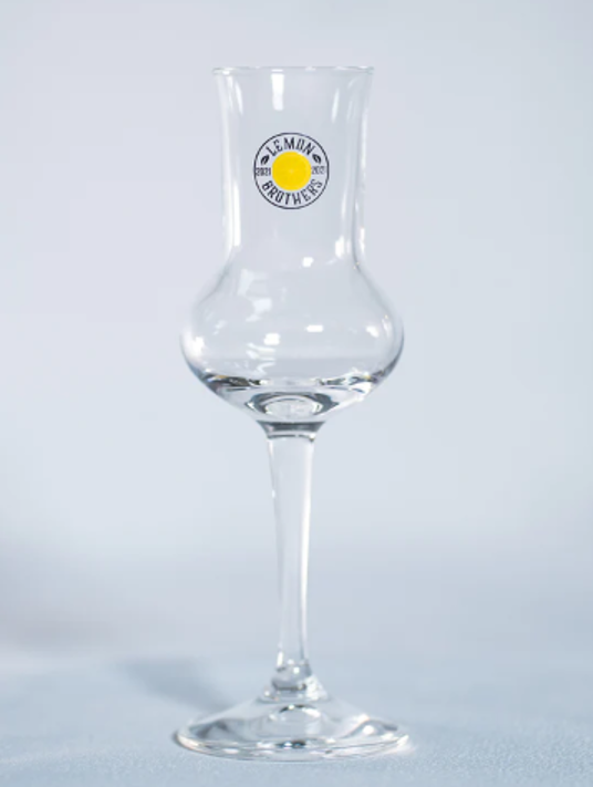 Single empty Lemon Brothers’ branded crystal glass on a light surface and background.