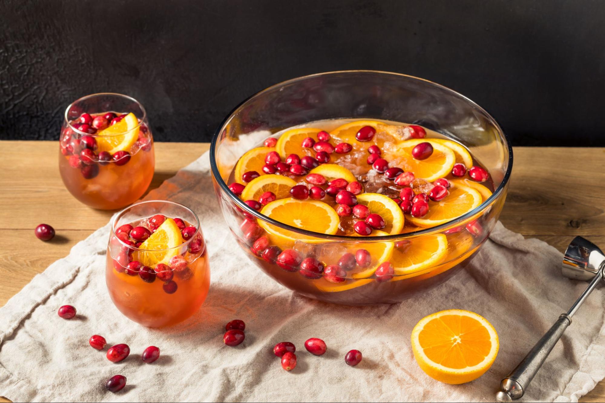 Punch bowl and two tumbler glasses full of Winter Citrus Limoncello Punch garnished with citrus slices and cranberries on a rustic tea towel.