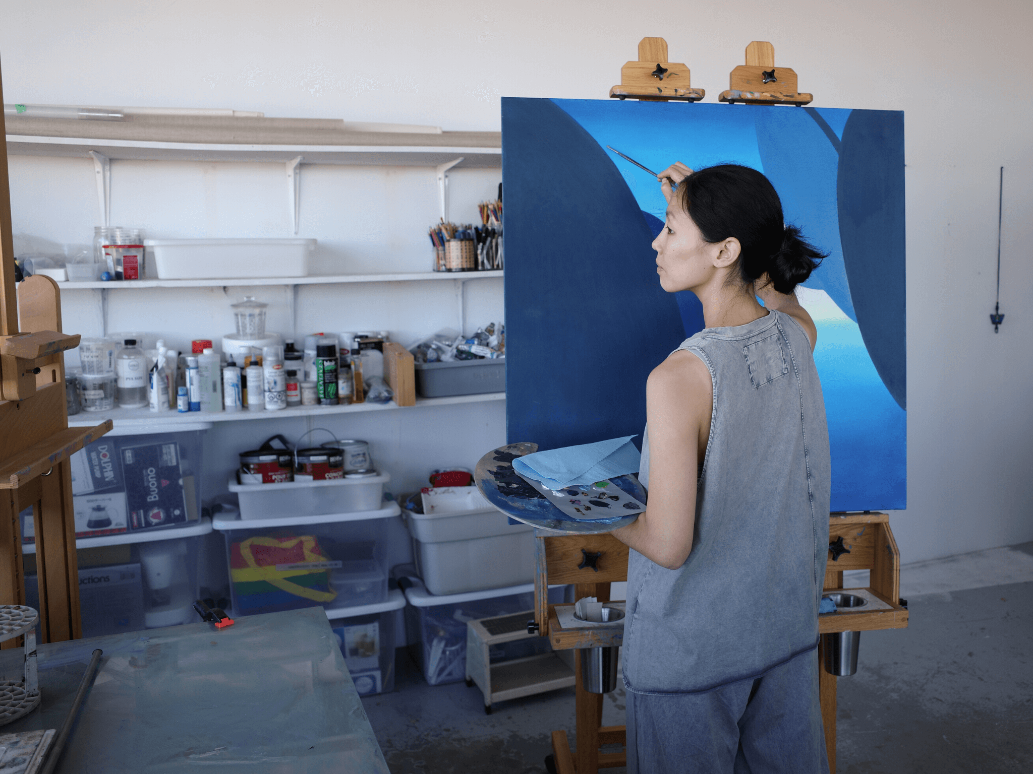 Jessica is in her studio working on a canvas with beautiful blues, and wearing a Totum over tank in washed grey. 