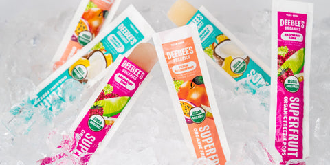 An image of six DeeBee’s Organics Tropical SuperFruit Freezie Pops standing atop a bed of ice. Three of the delicious freezie pops are open, and ready to eat.