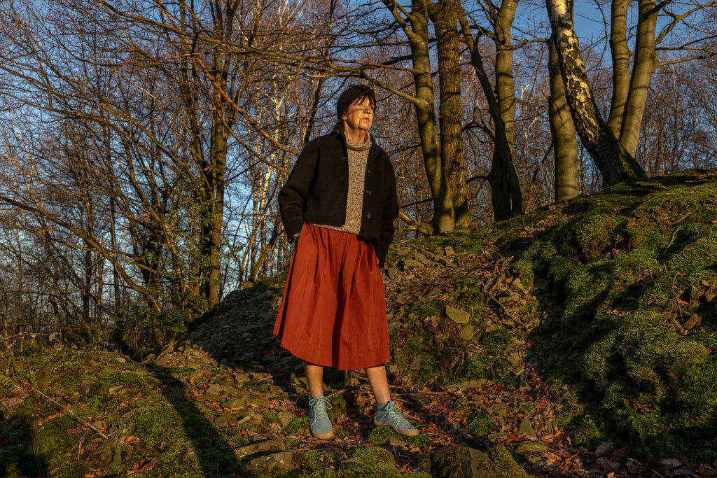 A person in front of still bare trees in the sunshine. They are wearing Wildling barefoot shoes.