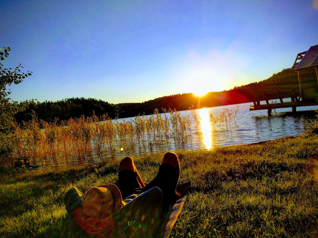 Sunset on a lake shore in the midst of untouched nature. In the foreground is a pair of crossed legs from feet to thighs.