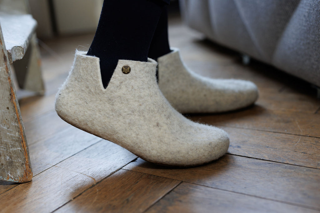 Side close-up of feet in Wildling Shoes slipper model Lotus made of light gray wool.