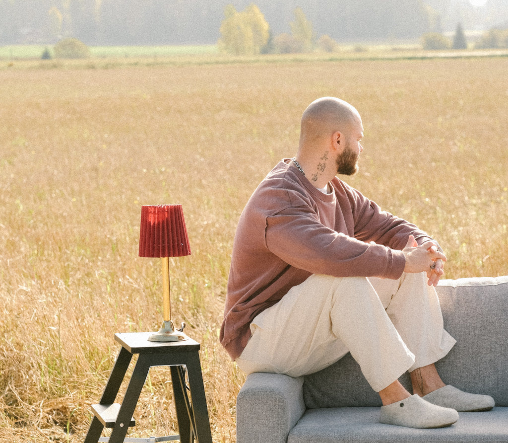 A person wearing Nelus, sitting on a grey couch which is standing in a cornfield