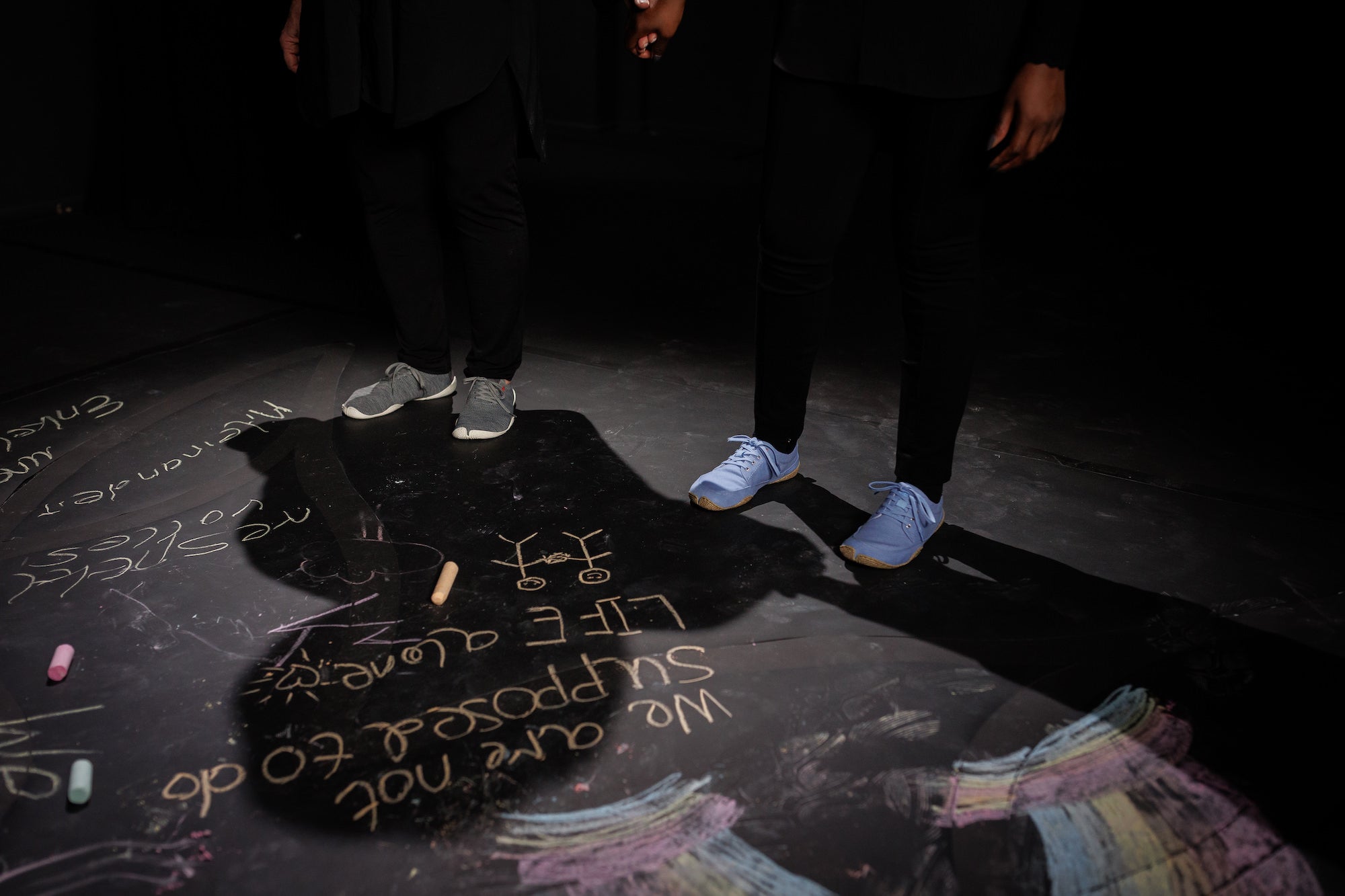 two people wearing wildling shoes standing on a black floor with colorful chalk drawings