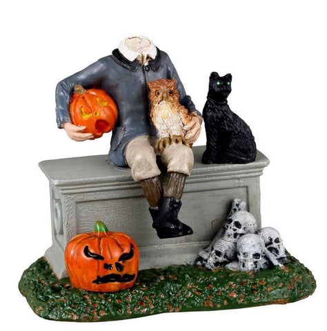 This Spooky Town figurine takes losing your head to a whole new level. Sitting atop a coffin that may or may not contain his missing head, this headless fellow is accompanied by a cat and owl who don't seem to be doing much to help him find his missing head. Perhaps he is just taking a break from searching and is contemplating using the jack o' lantern he holds as his new head. After all, anything can happen in Spooky Town.