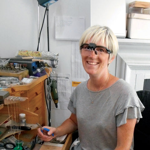 Woman sitting at jewellery work bench wearing specialist jeweller's goggles