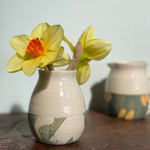 daffodils in a small ceramic vase with a small ceramic jug in the background 