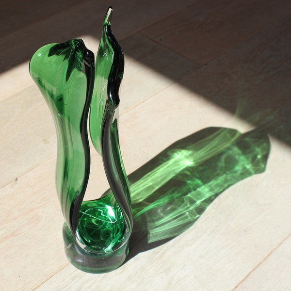 Tall green glass sculpture by glass artist Benjamin Lintell photographed in the sunlight so it casts a bright green shadow onto the floor 