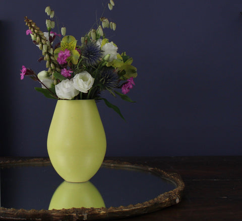 Yellow vase with flowers sitting on a mirror 