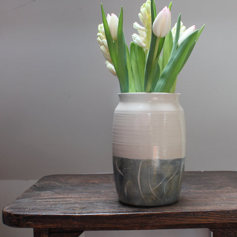 white tulips in a ceramic vase with a green glaze to the lower half sitting on a wooden table