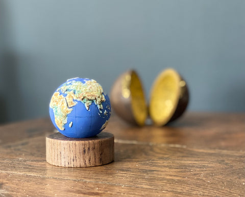 miniature blue and yellow globe on a wooden stand with its round box in the background it was made by loraine Rutt of the little globe company 