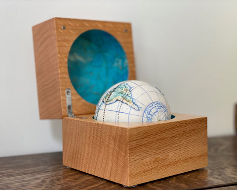 a small globe in a wooden box with the inside of the lid painted blue it was made by Loraine Rutt of the Little Globe company 